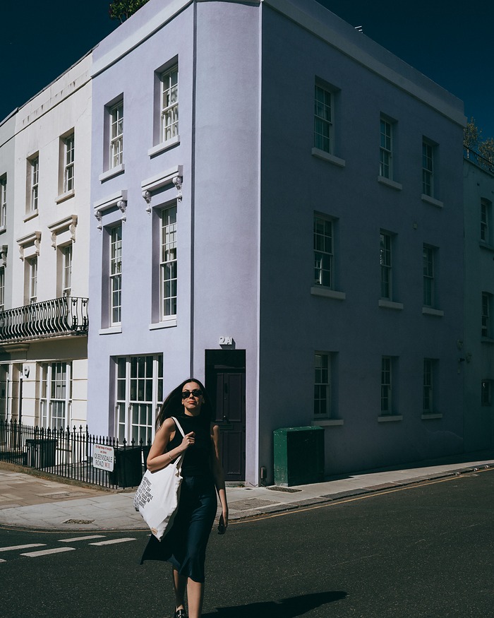 Woman in black crossing a Notting Hill street by a lilac corner house