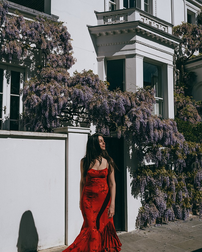 Woman in a red dress on the pavement under wisteria in Notting Hill