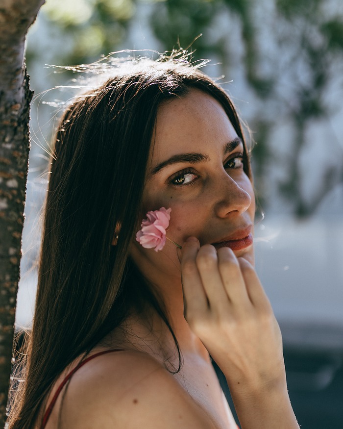 Close-up of a woman holding a cherry blossom against her cheek