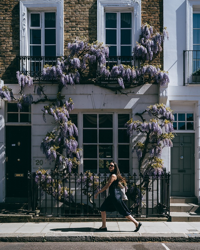 Woman in black walking past a white house covered in wisteria