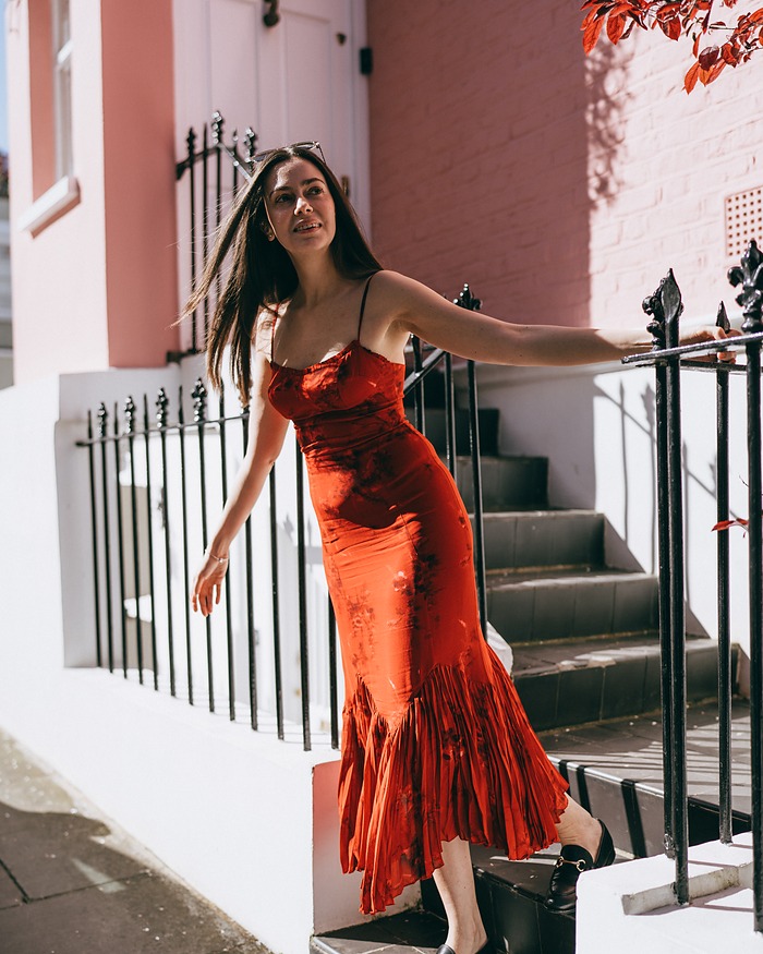 Woman in a red dress on the steps of a pink Notting Hill house