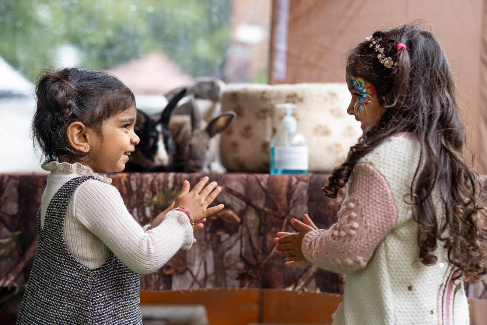 Two little girls touching hands at a birthday party, one with face paint