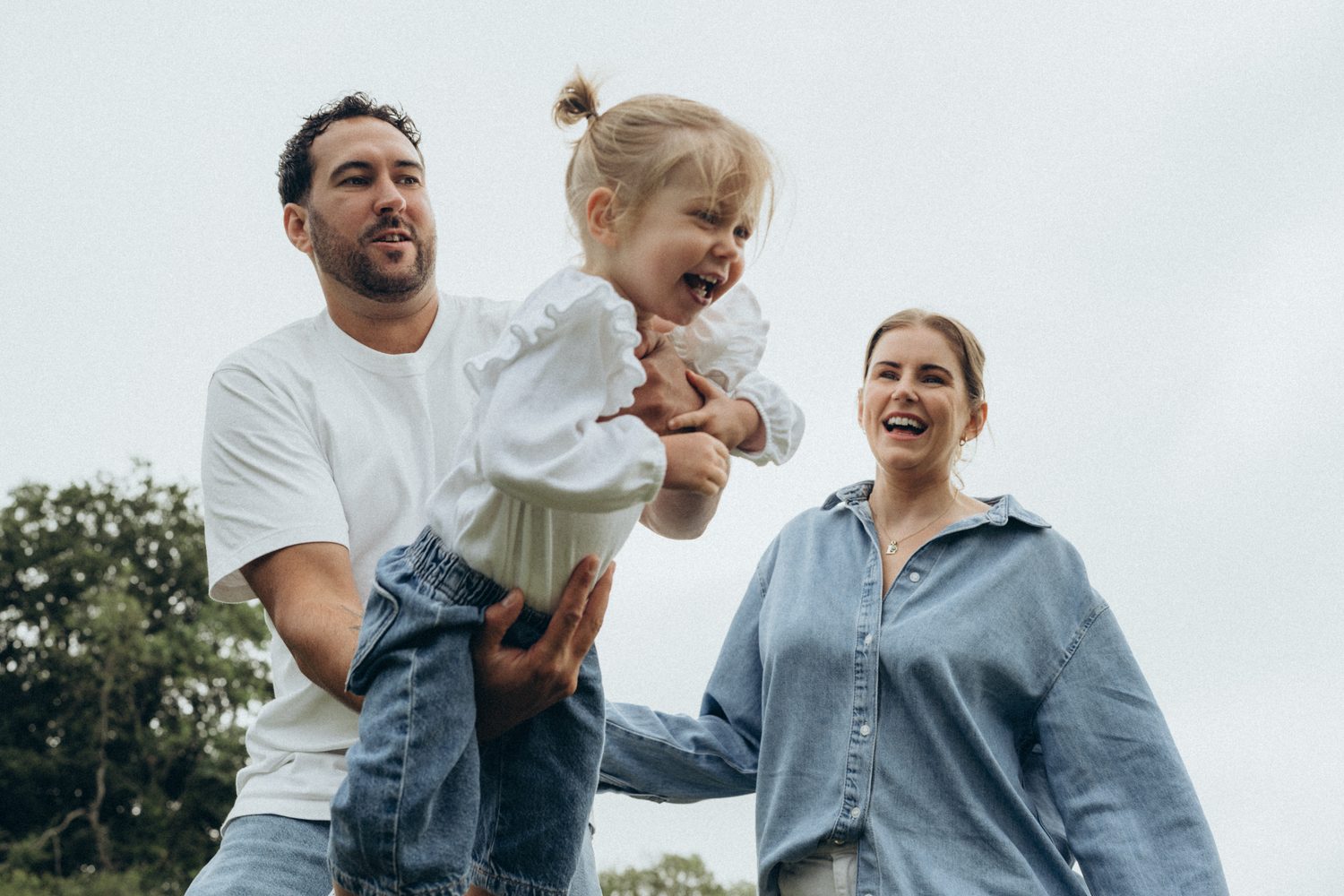 Parents swinging their laughing daughter in the air on a Surrey family shoot