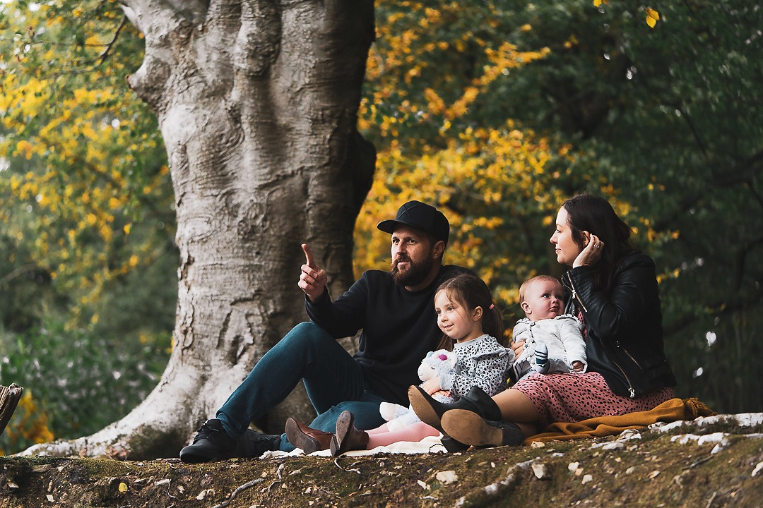 Family of four sitting beneath a huge old tree in autumn colour