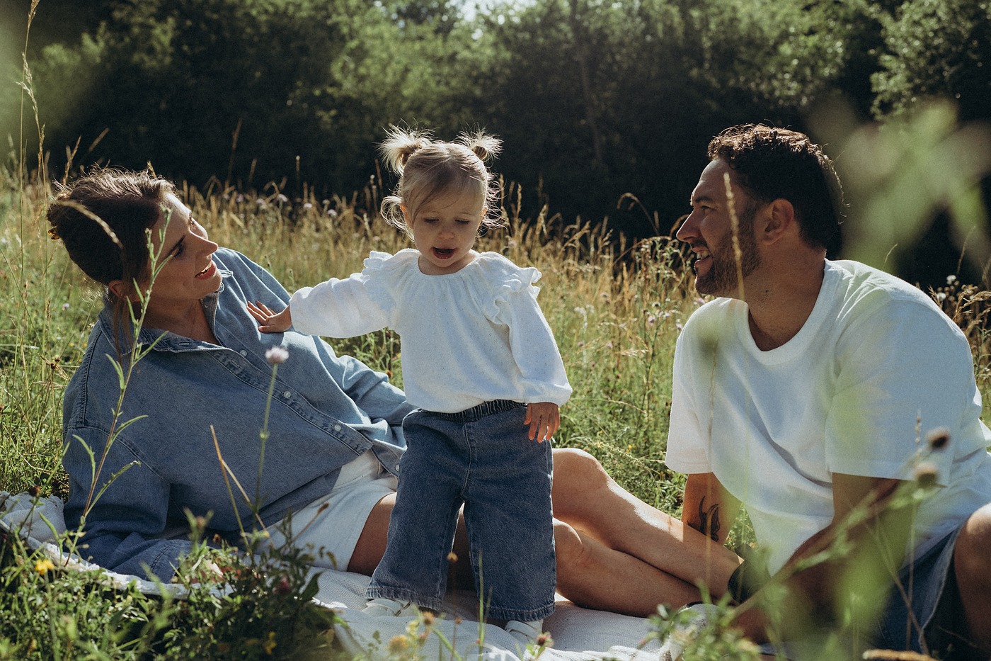 Family of three sitting together on a blanket in long grass