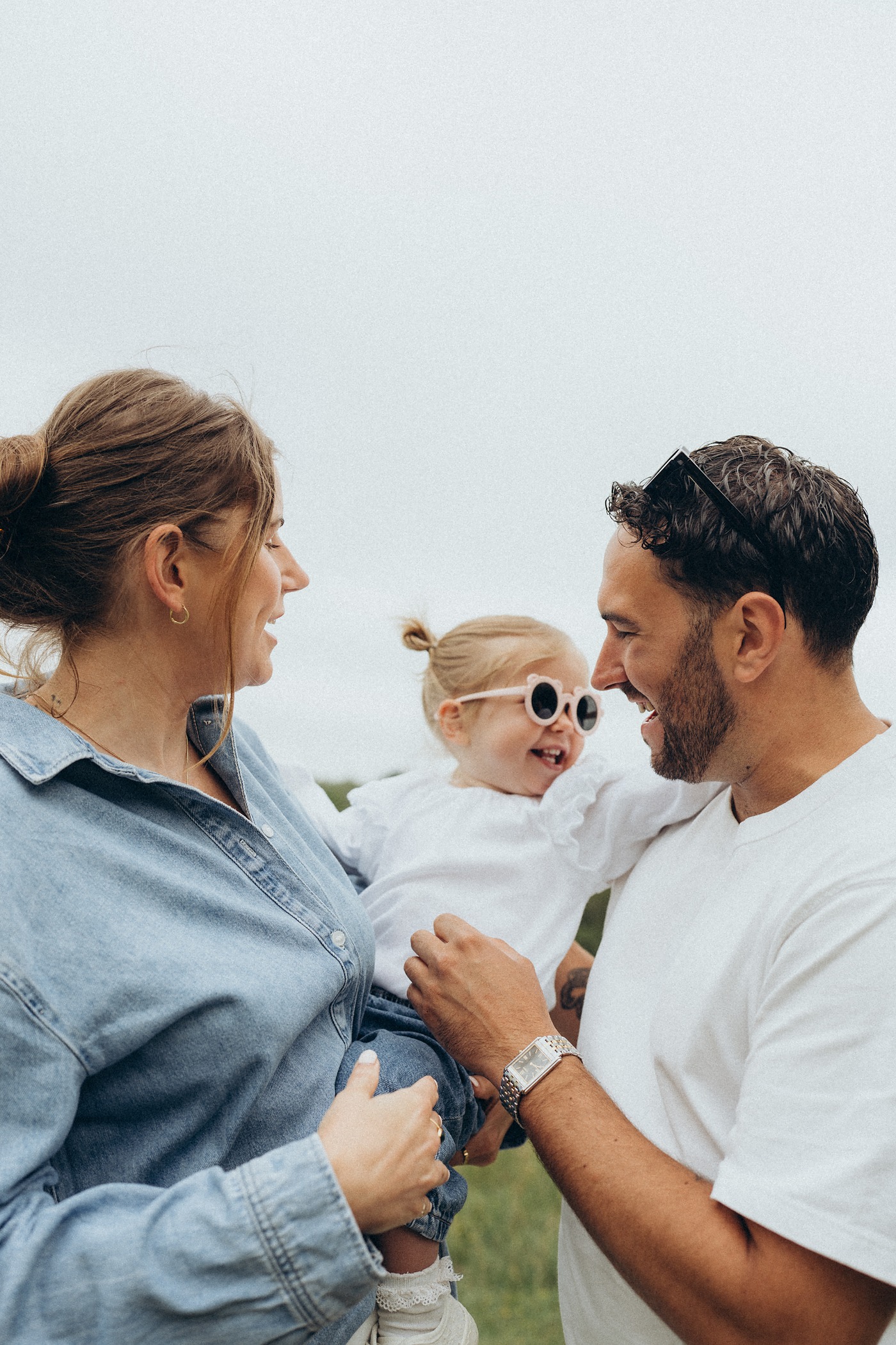 Mum and dad smiling at their toddler in round white sunglasses