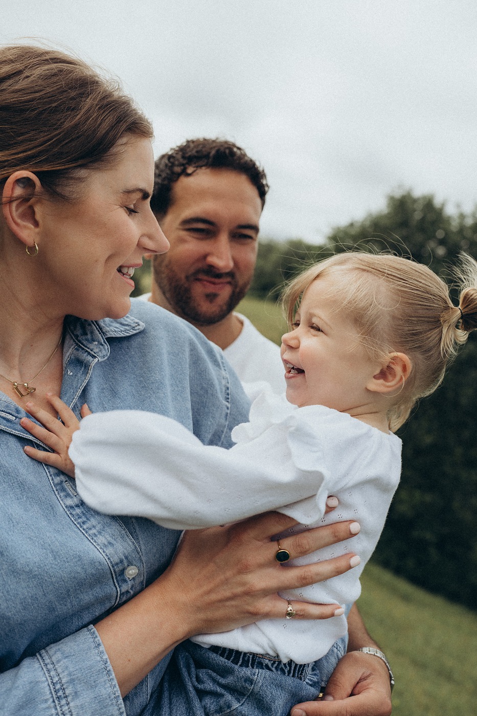 Mother and father holding their toddler between them in a field