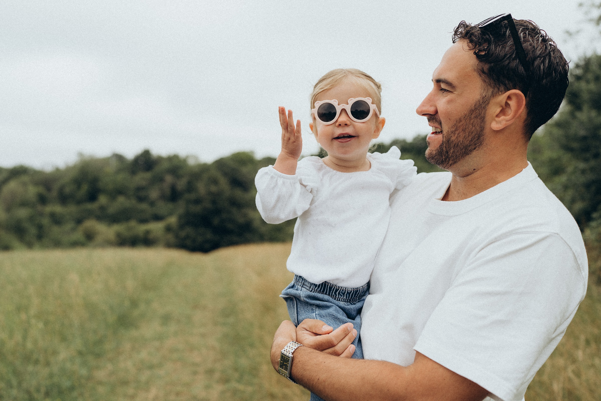 Father holding his toddler daughter in round sunglasses in an open field