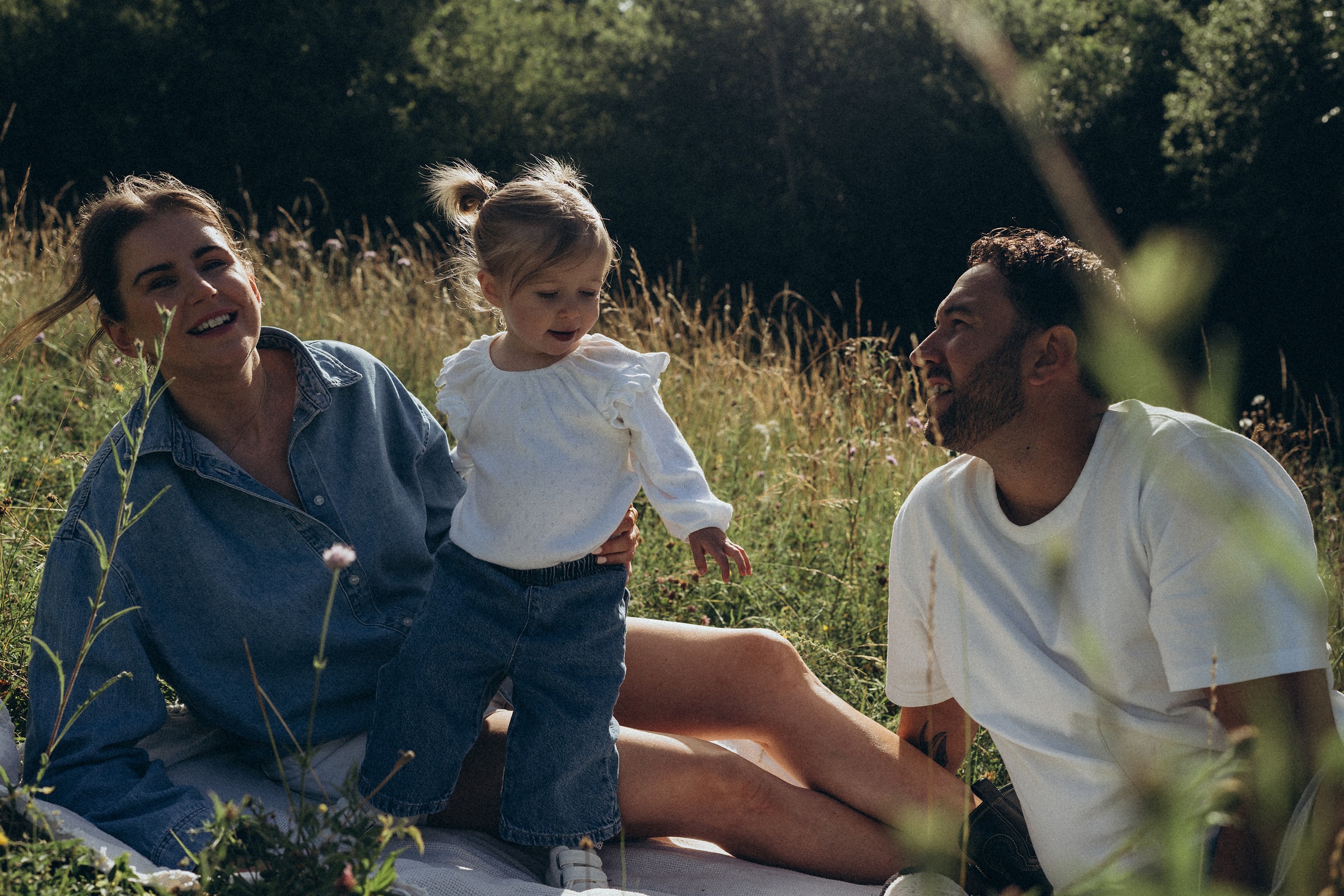 Family of three sitting together in long grass at the end of the day