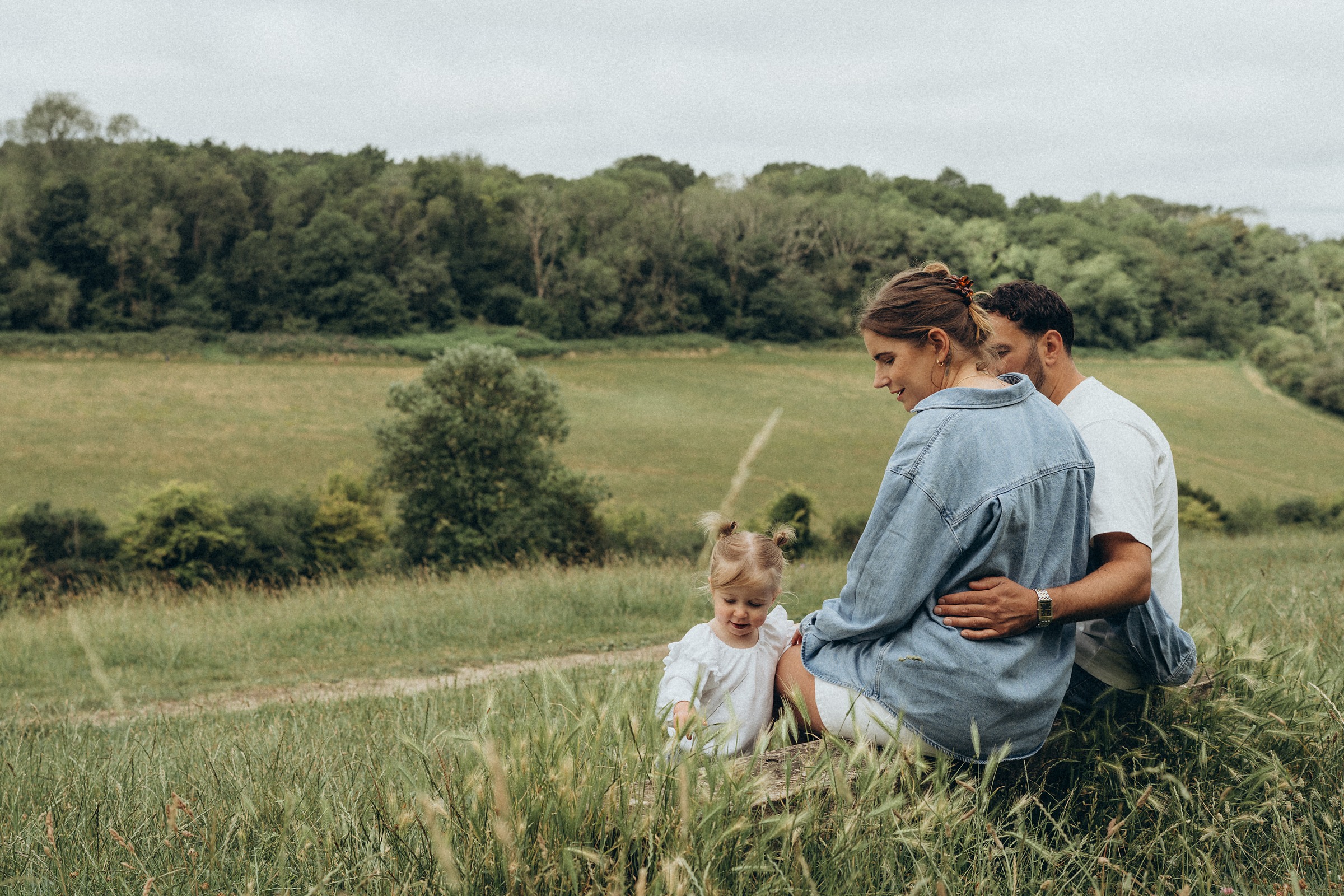 Family sitting together in a wide meadow with rolling countryside behind them