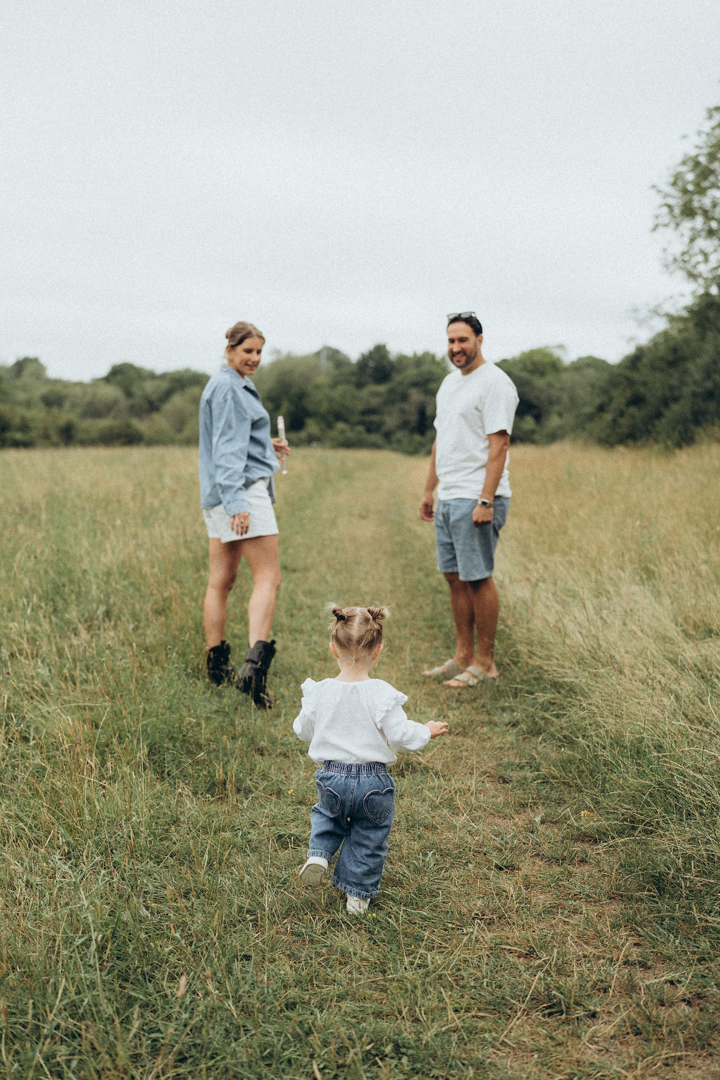 Toddler walking along a mown path towards her parents in a meadow