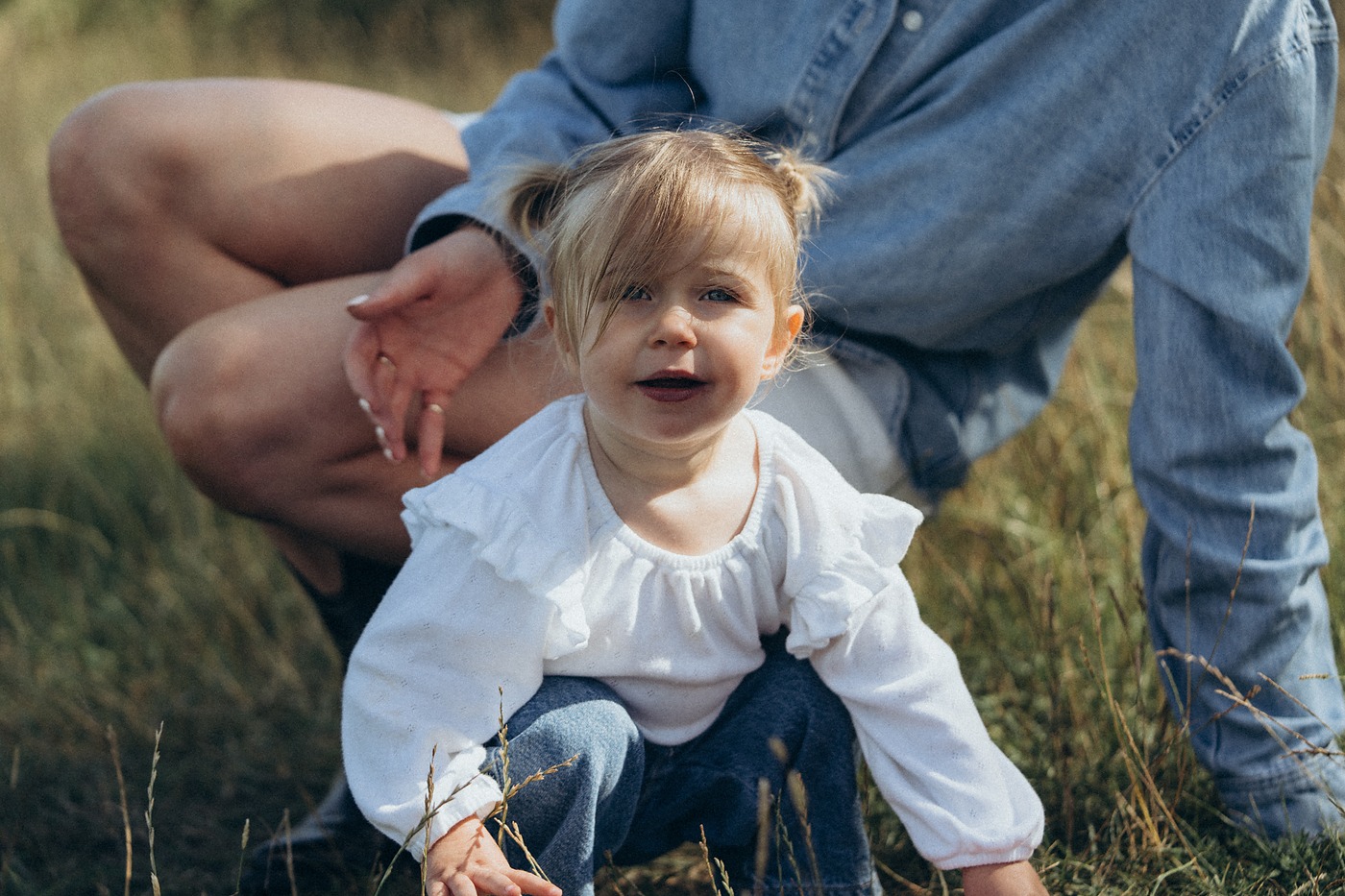 Toddler standing between her father's knees in a meadow