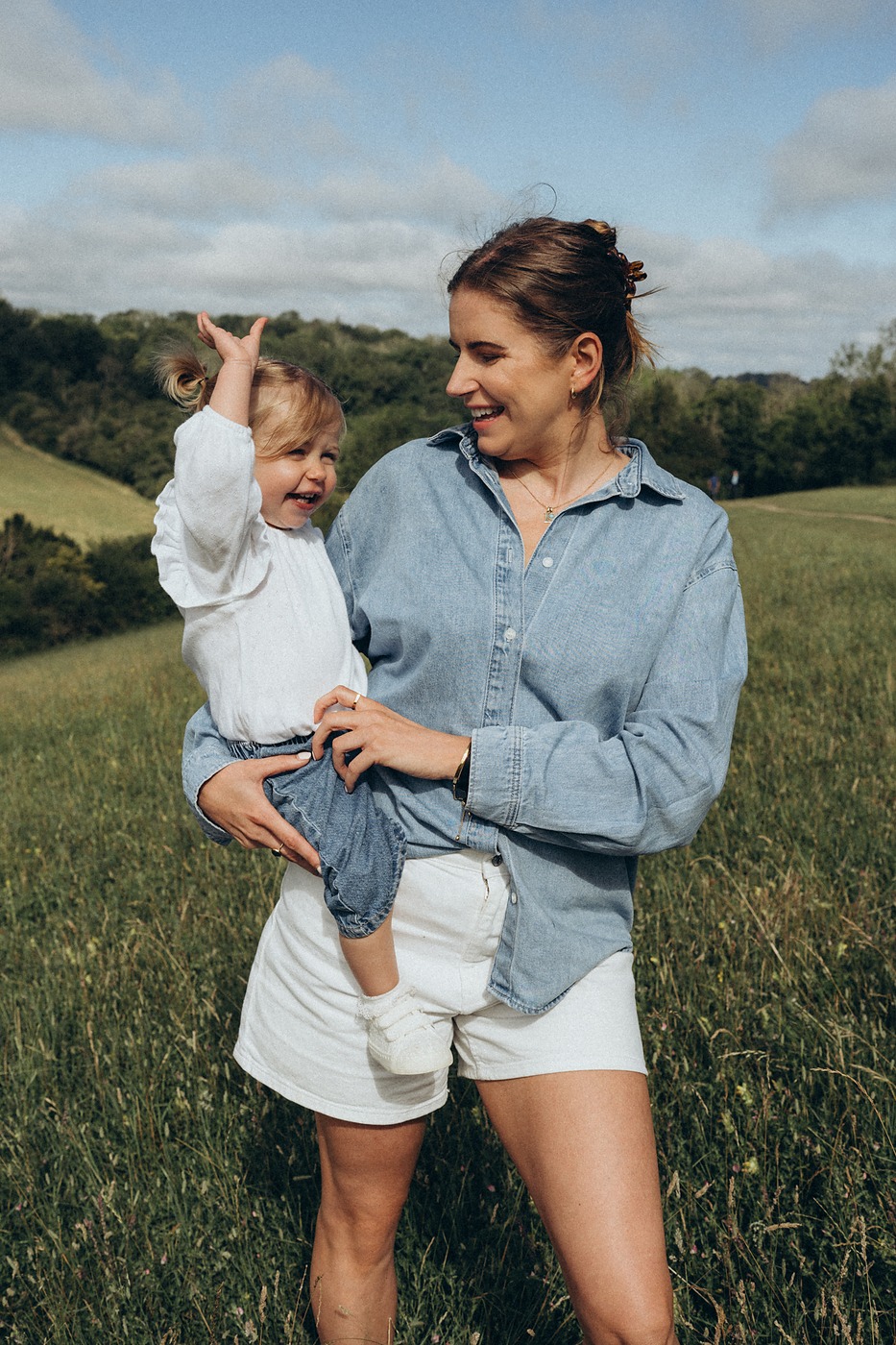 Mother lifting her toddler daughter up in a sunlit meadow