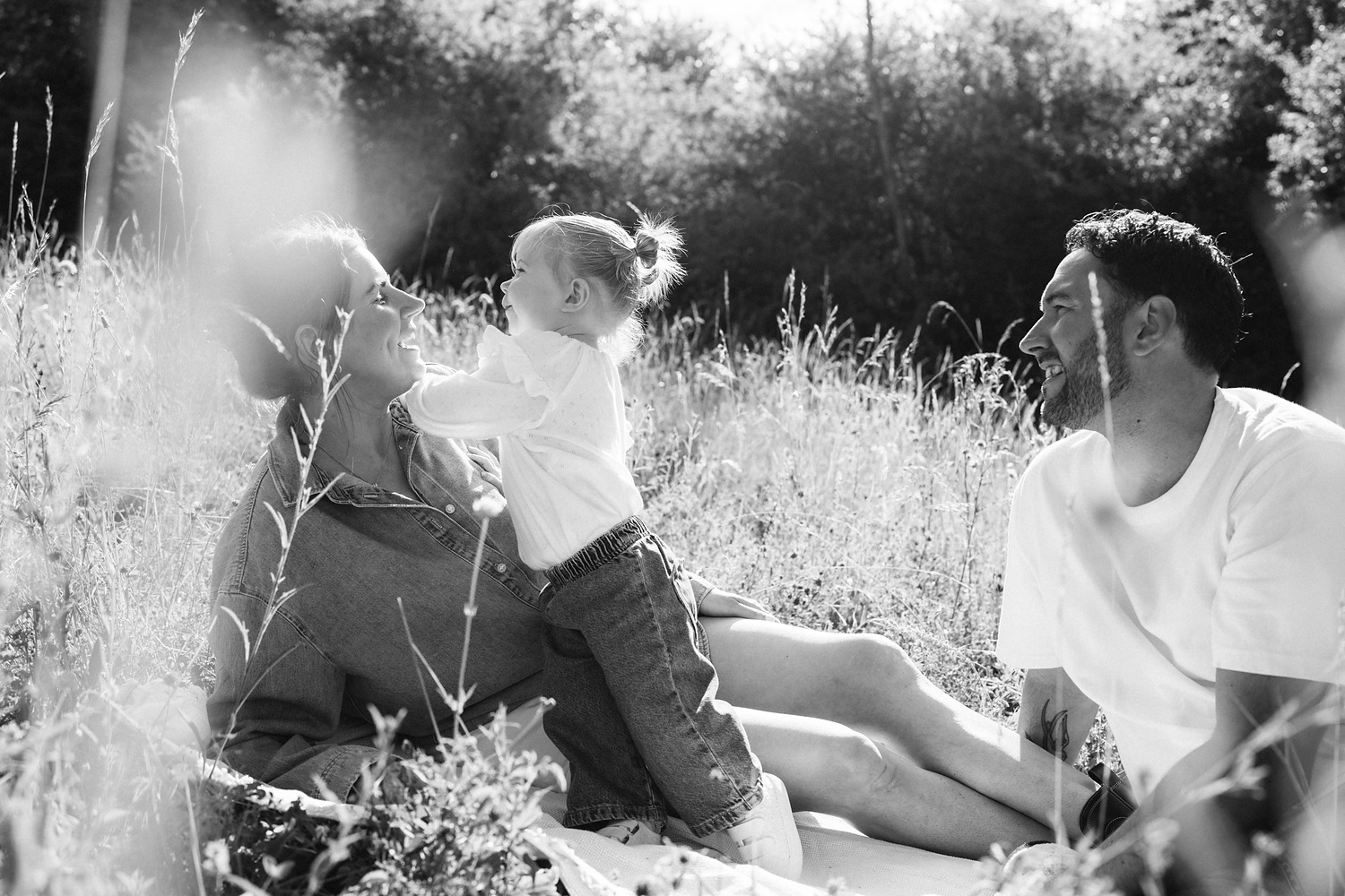 Black and white photo of parents playing with their toddler in the long grass