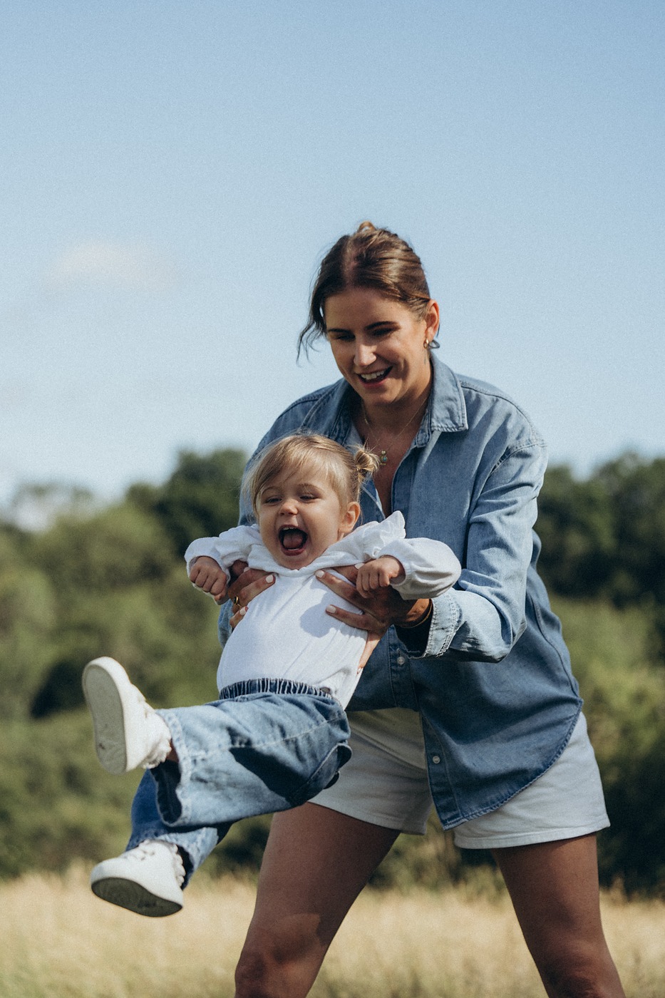 Mother swinging her toddler through long grass