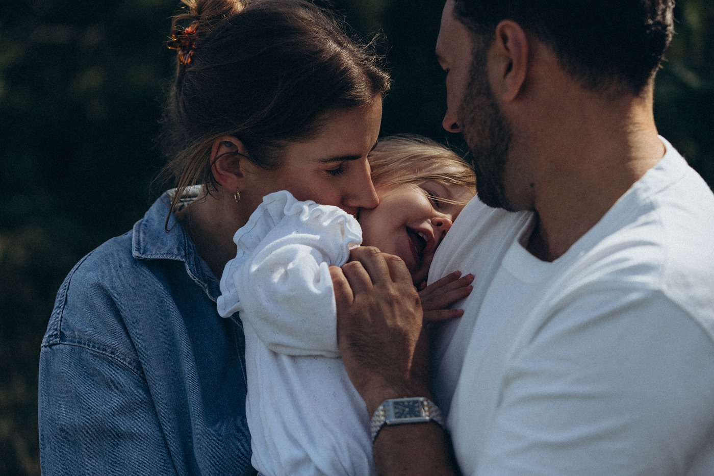 Parents leaning in to kiss their toddler daughter