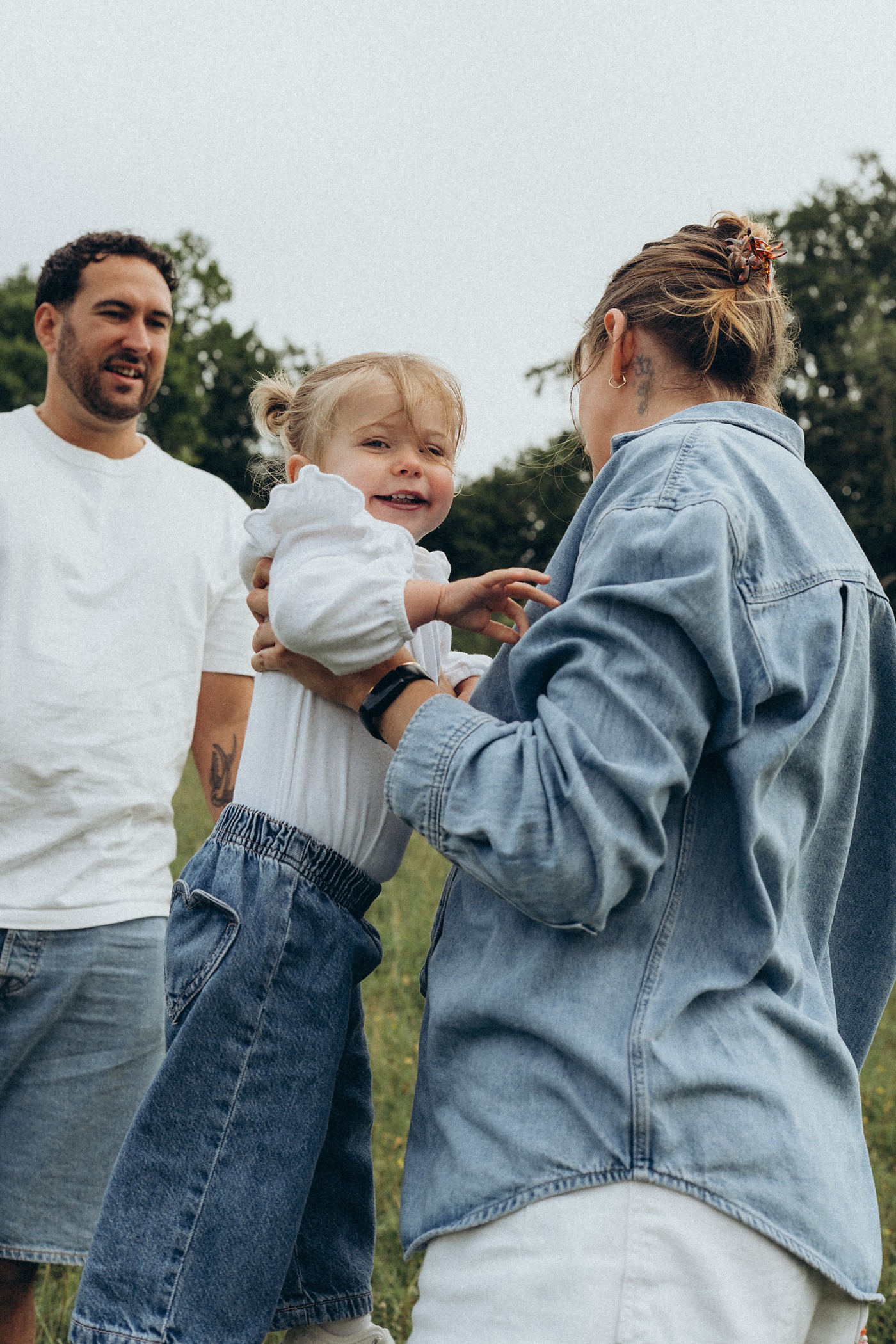 Toddler in her mum's arms reaching towards her dad