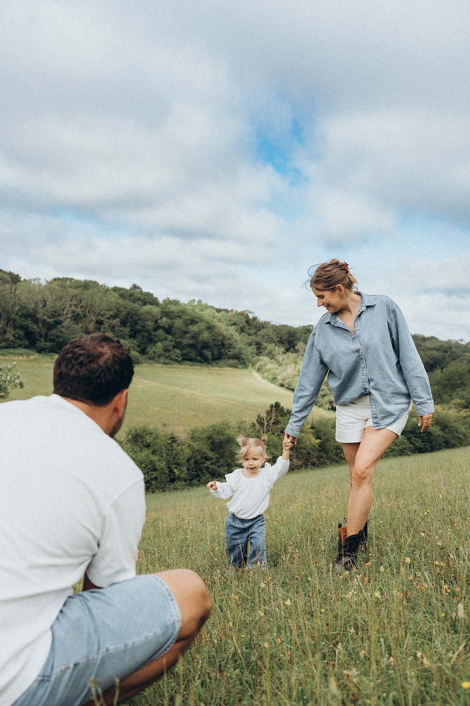 Father watching his toddler run ahead up a grassy hill