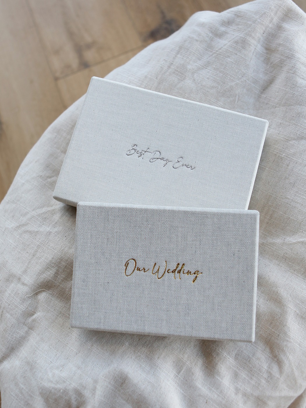 Two cream keepsake print boxes with gold lettering resting on linen