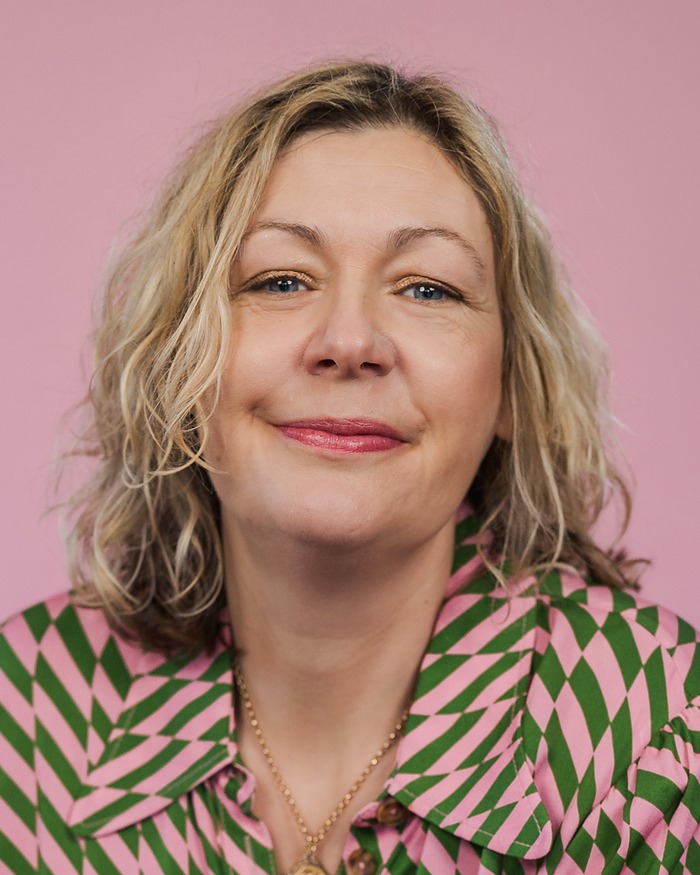 Headshot of a smiling woman with curly blonde hair against a pink backdrop
