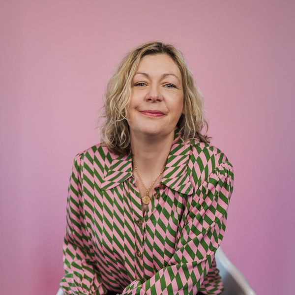 Woman in a patterned blouse smiling in front of a pink wall