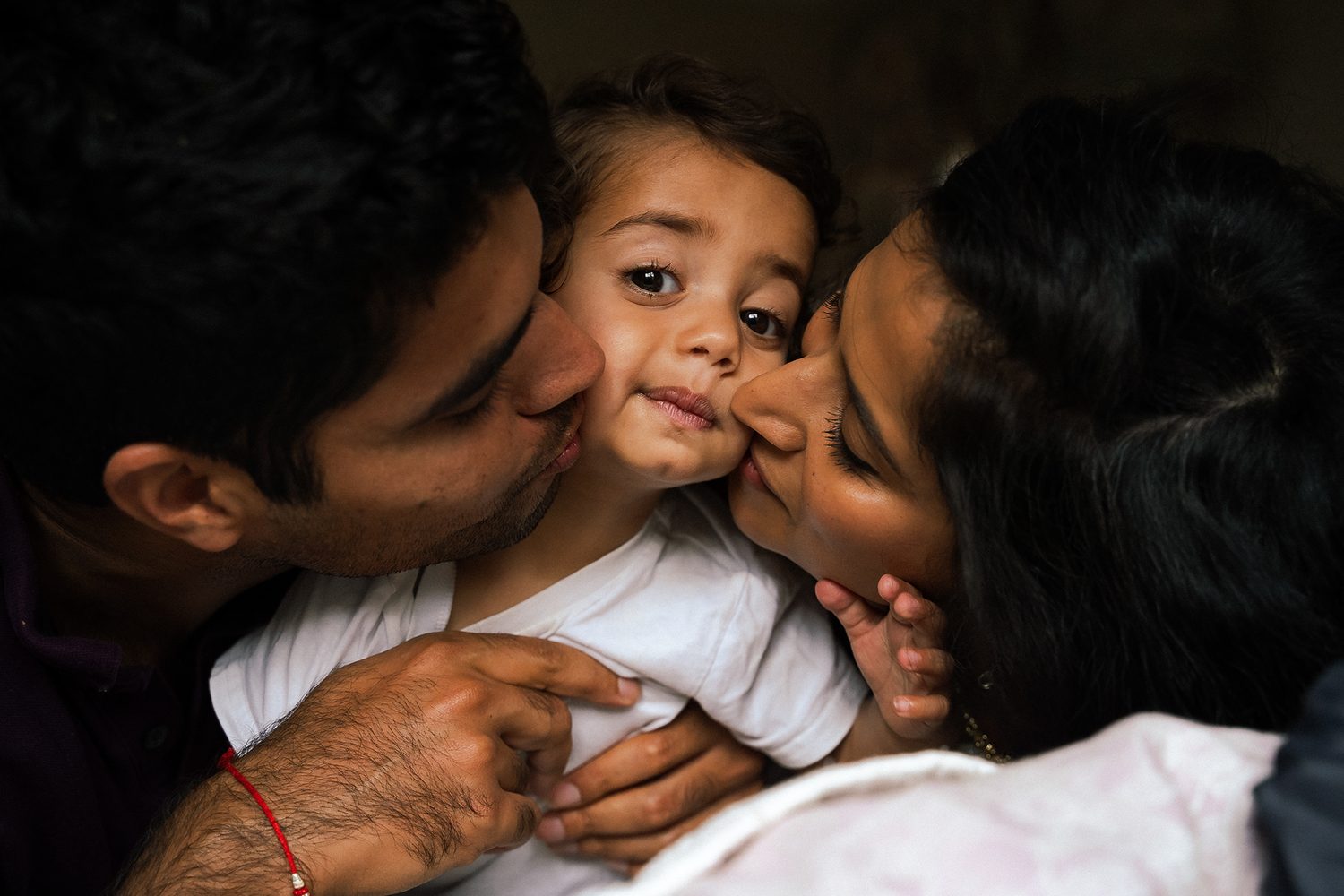 Parents kissing their toddler on both cheeks at home in Surrey