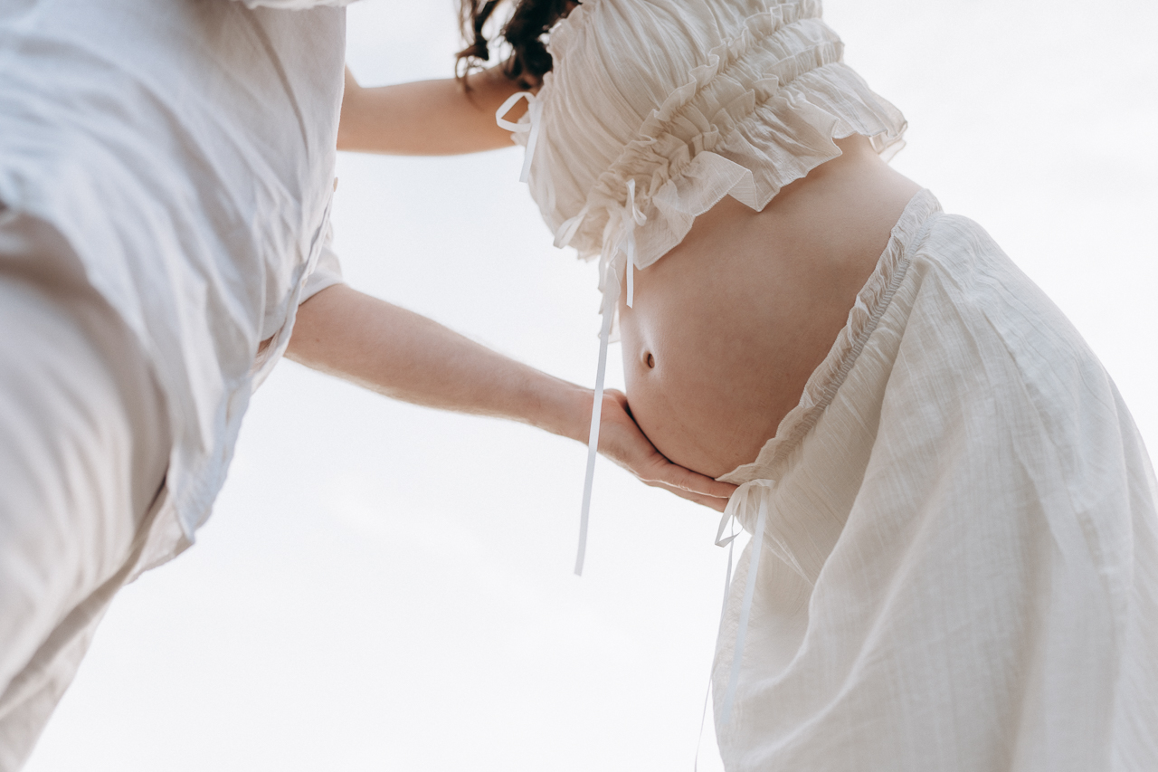 Partner cradling the bump during an outdoor maternity session in Surrey