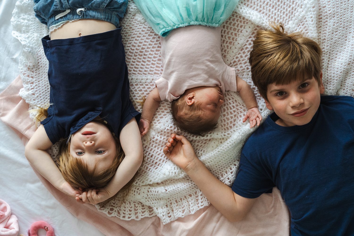 Three children lying together at a newborn session at home in Surrey