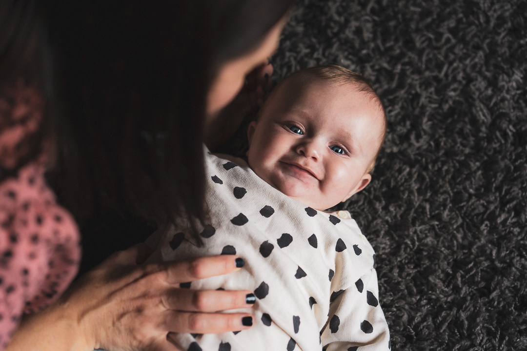 Baby smiling over their mother's shoulder at home in Surrey