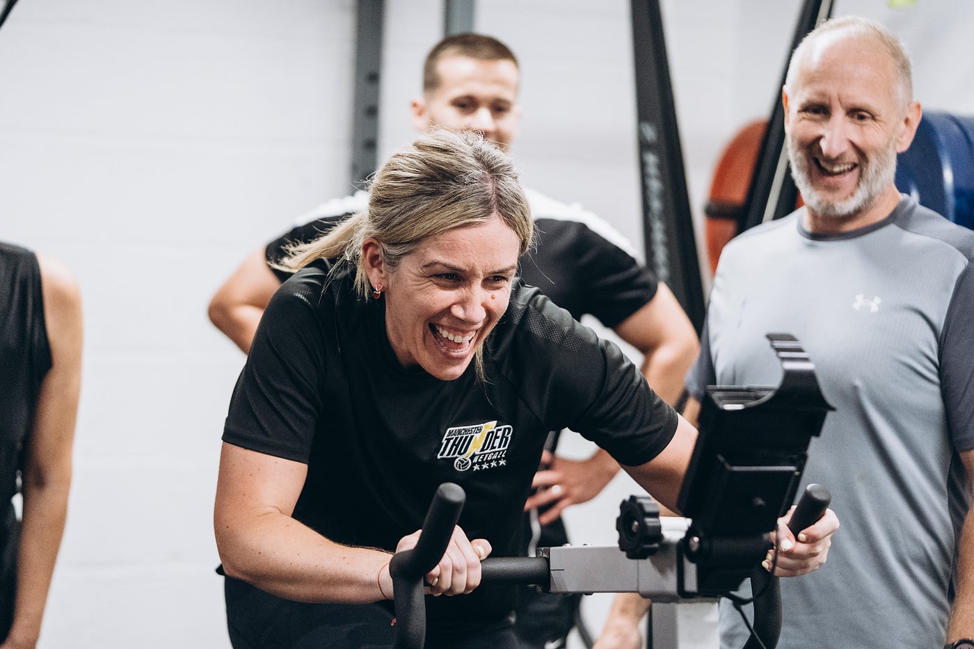 Woman laughing on the bike while two teammates cheer beside her