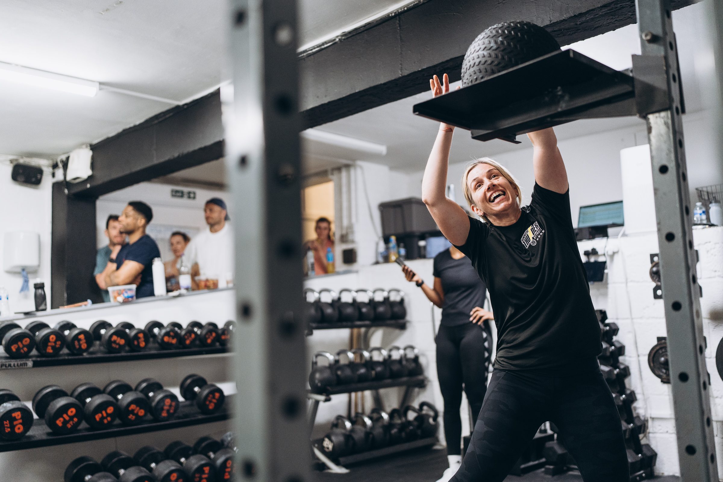 Woman laughing as she lifts a heavy ball onto a platform at the SSP Team Games in Caterham