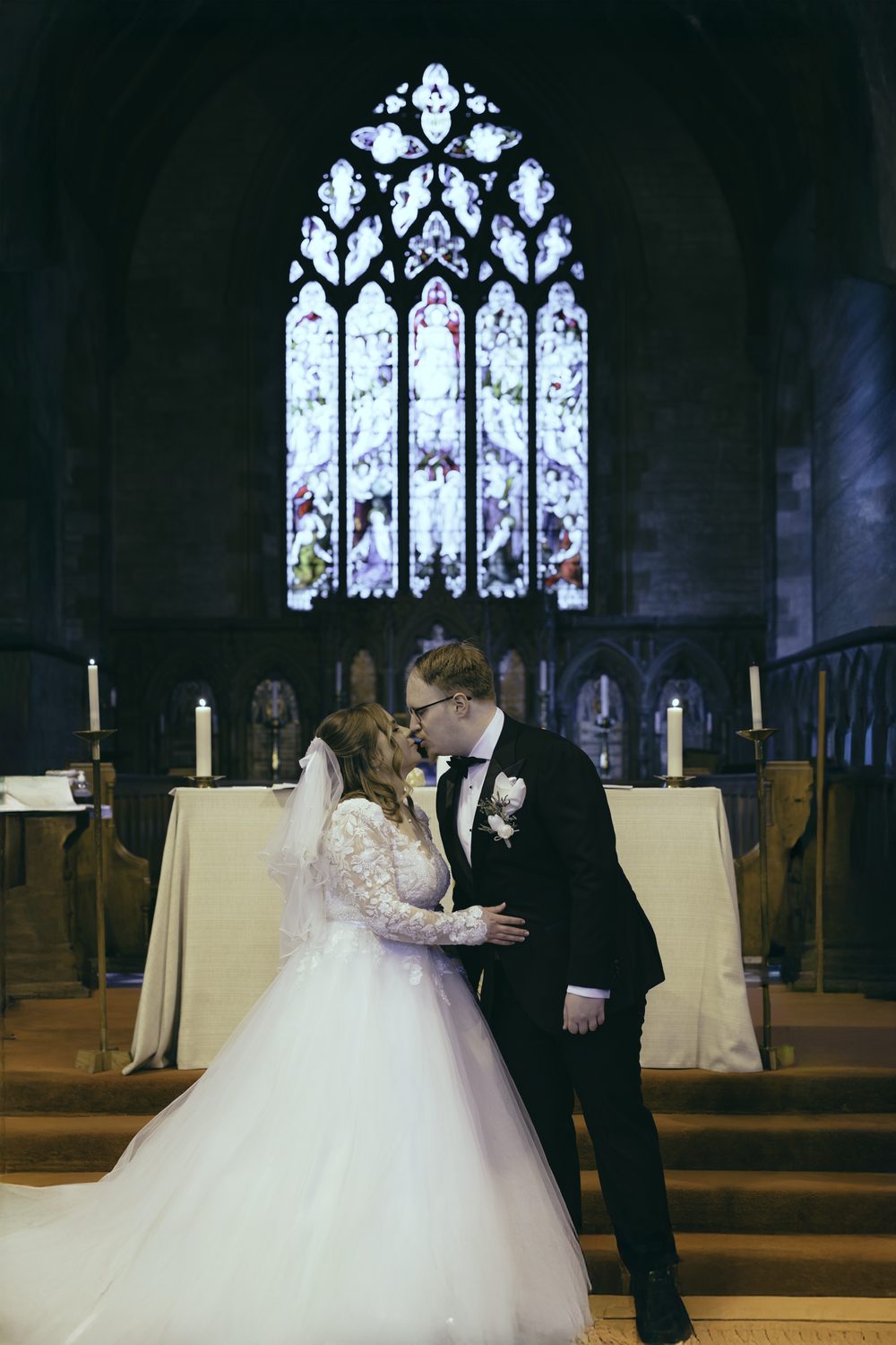 Newlyweds kissing beneath the stained glass window at St. John the Evangelist, Caterham Valley