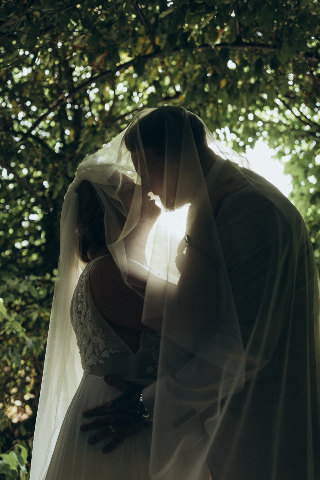 Bride and groom kissing behind a backlit veil in low light
