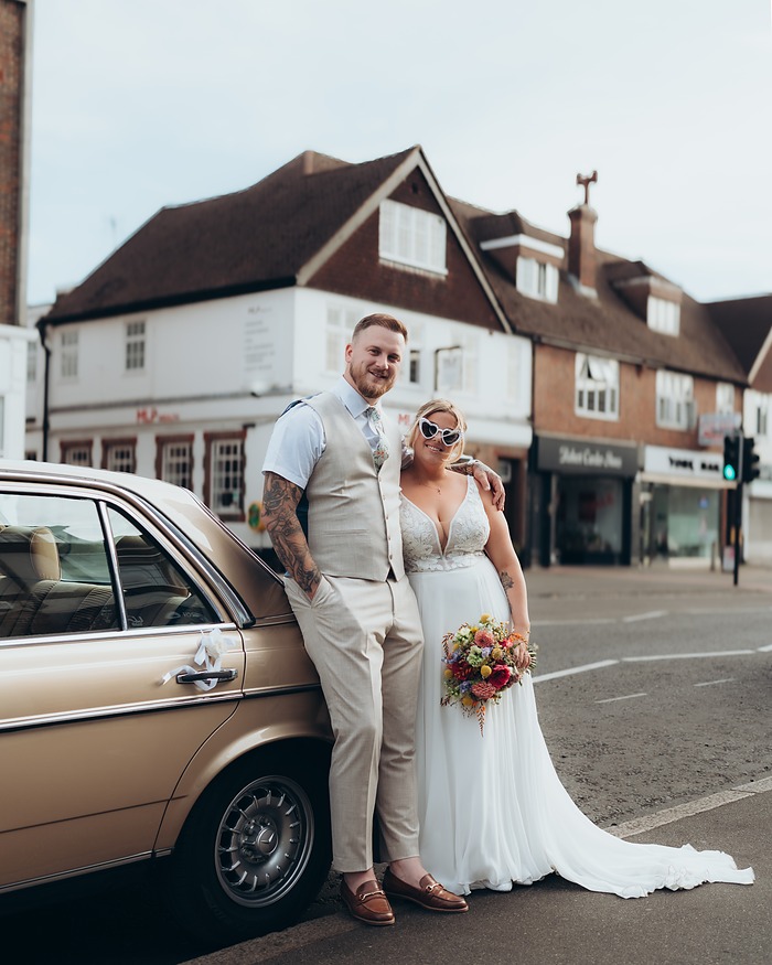 Bride and groom beside a vintage car on a Surrey street