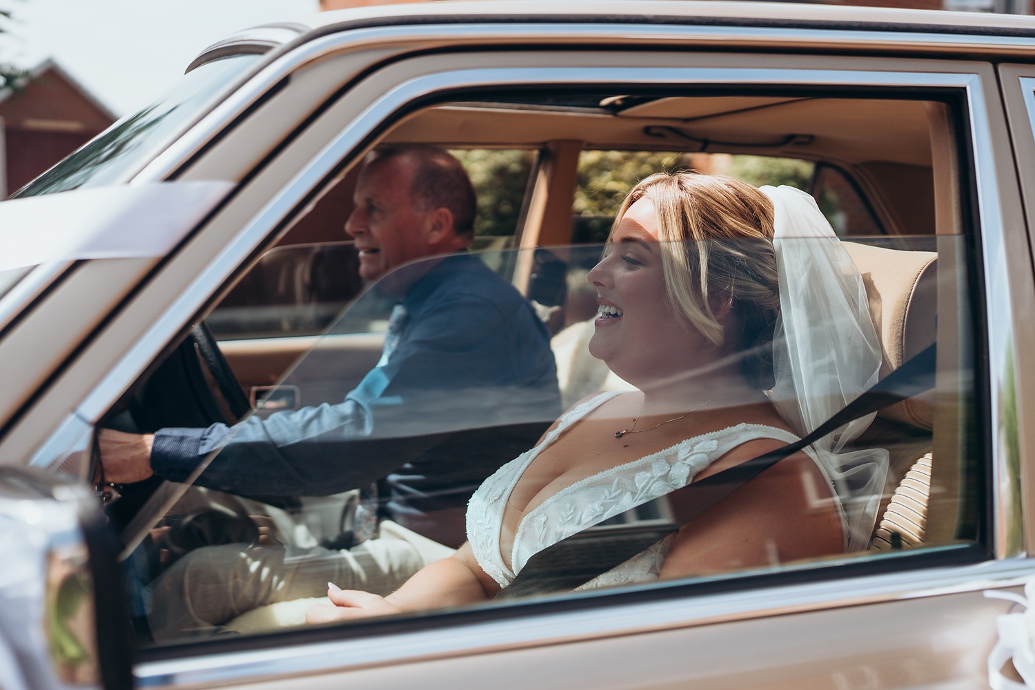 Laughing bride in her veil being driven to her wedding in a vintage car