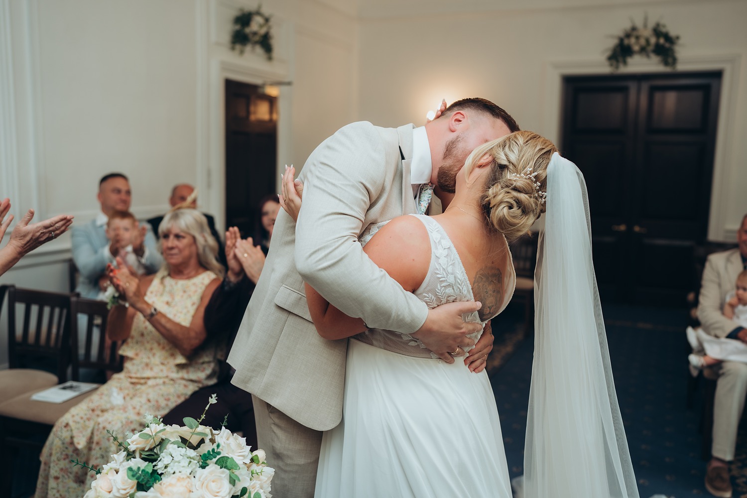 Newlyweds sharing their first kiss as their guests applaud