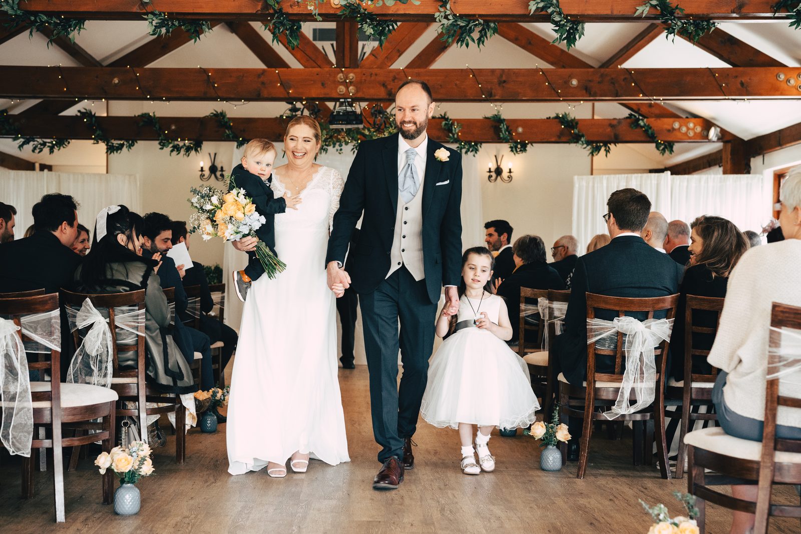 Bride and groom walking back down the aisle of a timber-beamed venue as their guests look on